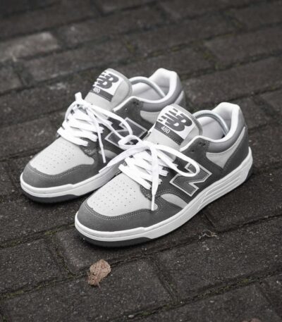 A pair of grey and white New Balance 480 sneakers on a brick floor, perfect for men looking for stylish and comfortable footwear.