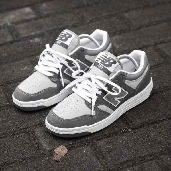 A pair of grey and white New Balance 480 sneakers on a brick floor, perfect for men looking for stylish and comfortable footwear.