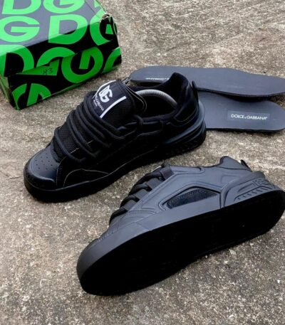 A pair of black Dolce & Gabbana sneakers with box and insoles on a concrete floor, perfect for stylish men in Nigeria.