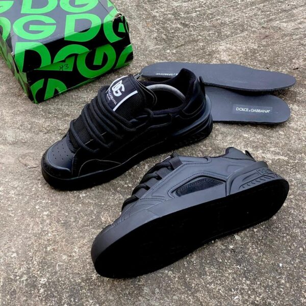 A pair of black Dolce & Gabbana sneakers with box and insoles on a concrete floor, perfect for stylish men in Nigeria.