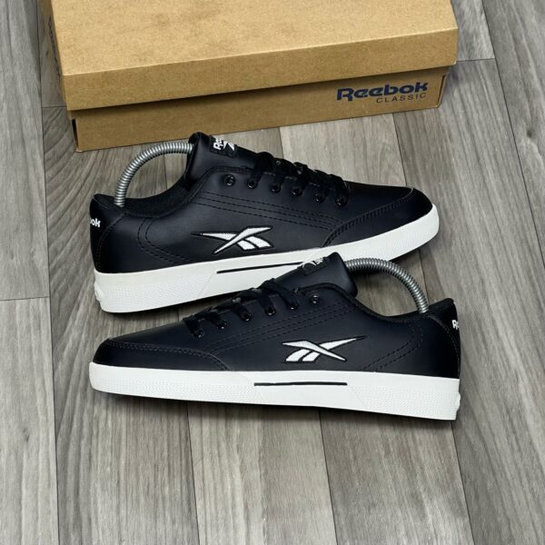 A pair of black and white Reebok Classic Leather sneakers with box on a wooden floor, perfect for men's casual wear.