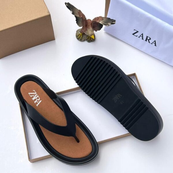 A pair of black T-strap flip flops with brown insole, placed on a white background with a shoe box and bag.