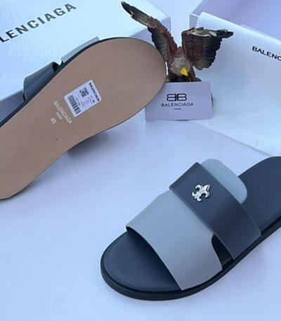 A pair of black and grey Balenciaga slide sandals with a white logo, displayed with their box and packaging.