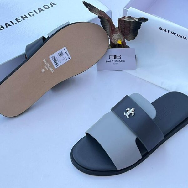 A pair of black and grey Balenciaga slide sandals with a white logo, displayed with their box and packaging.
