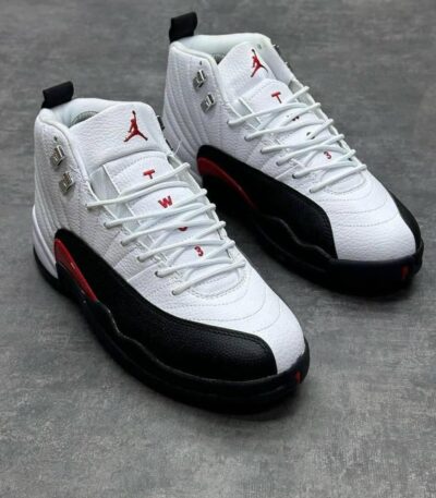 A pair of white, black, and red Air Jordan 12 Retro sneakers on a grey background, showcasing their sleek design and premium materials.