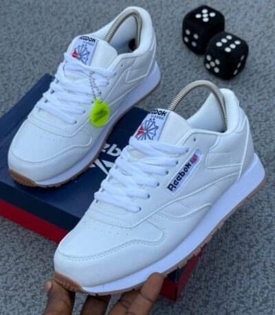 A pair of white Reebok Classic Leather sneakers on a grey background, showcasing the shoe's sleek design and comfort features.