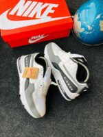 A pair of white and grey Nike Air Max sneakers with a red Nike shoe box and a blue globe in the background, showcasing the shoe's stylish design and comfort features.