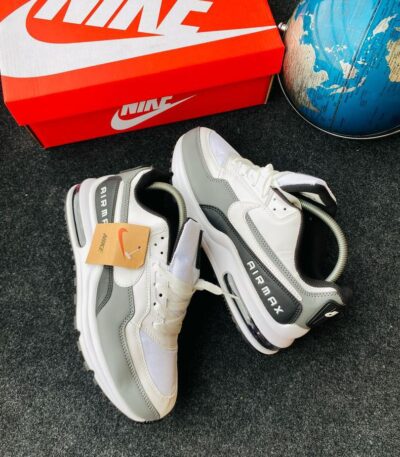 A pair of white and grey Nike Air Max sneakers with a red Nike shoe box and a blue globe in the background, showcasing the shoe's stylish design and comfort features.