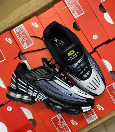 A pair of black and white Nike Air Max Plus sneakers on top of red shoe boxes, showcasing the shoe's sleek design and Tuned Air technology for ultimate comfort and style.