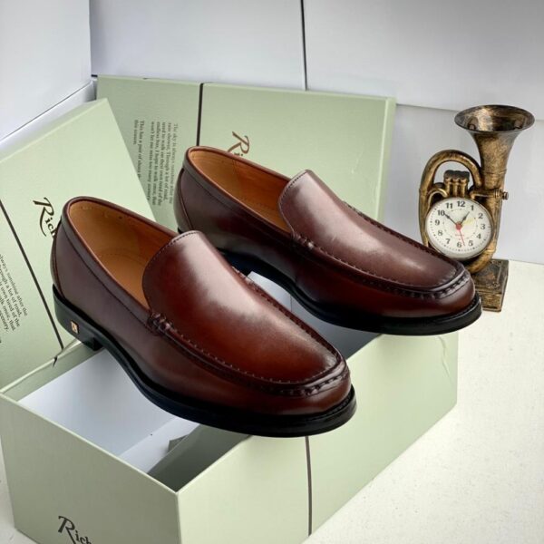 A pair of rich brown leather loafers on a shoe box with a clock in the background, showcasing stylish and comfortable footwear for men.