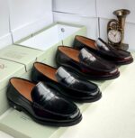 A pair of dark brown leather loafers from Richwanaz, displayed in an open box with a clock and other accessories.