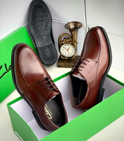 A pair of stylish brown leather oxford shoes displayed in a green box, showcasing their sleek design and luxurious texture.