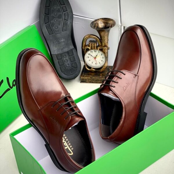 A pair of stylish brown leather oxford shoes displayed in a green box, showcasing their sleek design and luxurious texture.