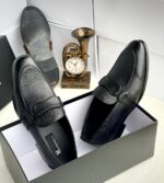 A pair of black leather loafers with perforated details in a shoe box, exuding luxury and sophistication.