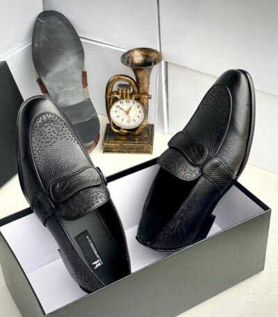 A pair of black leather loafers with perforated details in a shoe box, exuding luxury and sophistication.