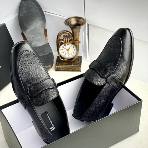 A pair of black leather loafers with perforated details in a shoe box, exuding luxury and sophistication.