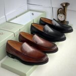 A pair of rich brown leather loafers on a shoe box with a clock in the background, showcasing stylish and comfortable footwear for men.