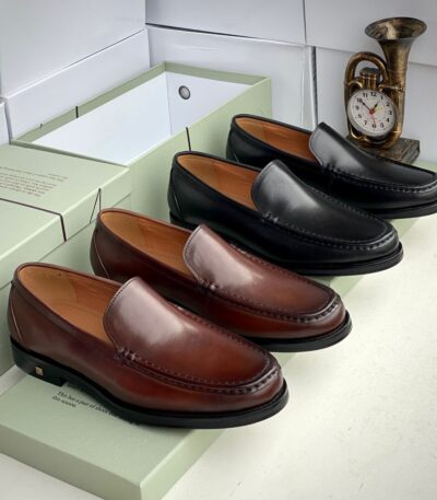 A pair of rich brown leather loafers on a shoe box with a clock in the background, showcasing stylish and comfortable footwear for men.