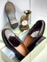 A pair of dark brown leather loafers from Richwanaz, displayed in an open box with a clock and other accessories.