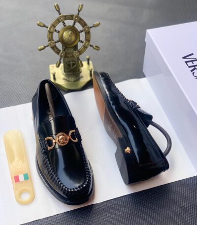 A pair of black leather loafers with gold-tone Medusa buckle, presented on a white shoe box with a luxurious background, showcasing the shoe's sleek design and premium materials.