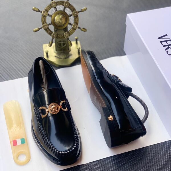 A pair of black leather loafers with gold-tone Medusa buckle, presented on a white shoe box with a luxurious background, showcasing the shoe's sleek design and premium materials.