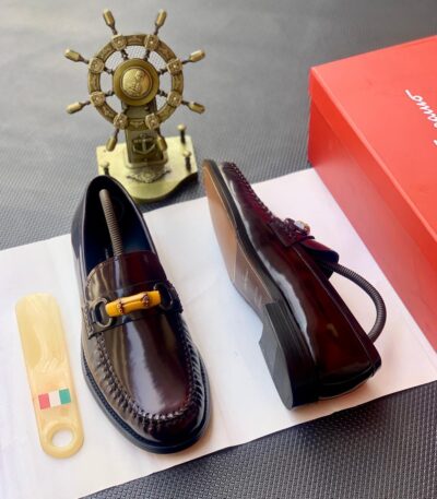A pair of dark brown leather loafers with tassel detailing, presented on a white paper with a shoe horn and red shoe box in the background, showcasing ArvoLuxury's commitment to premium footwear.