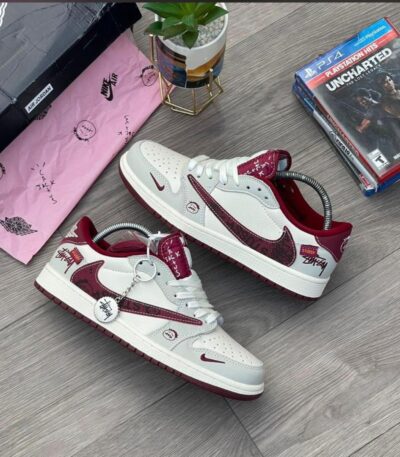 A pair of white and red Stussy x Nike Air Jordan 1 high top sneakers on a wooden floor, showcasing the unique design and style of the shoes.