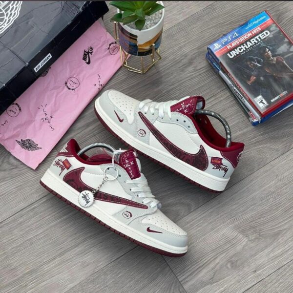 A pair of white and red Stussy x Nike Air Jordan 1 high top sneakers on a wooden floor, showcasing the unique design and style of the shoes.
