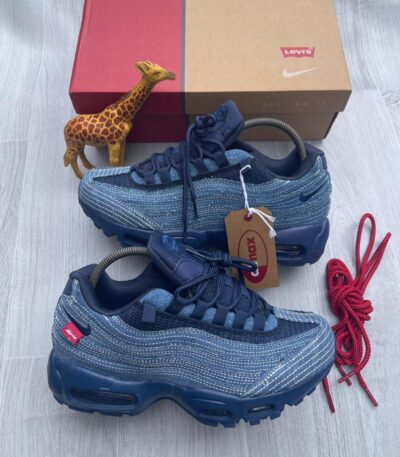A pair of denim blue Nike Air Max sneakers with red accents, displayed with a giraffe toy and shoe box on a light grey surface.