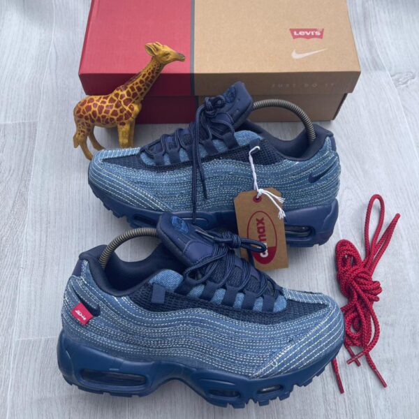 A pair of denim blue Nike Air Max sneakers with red accents, displayed with a giraffe toy and shoe box on a light grey surface.