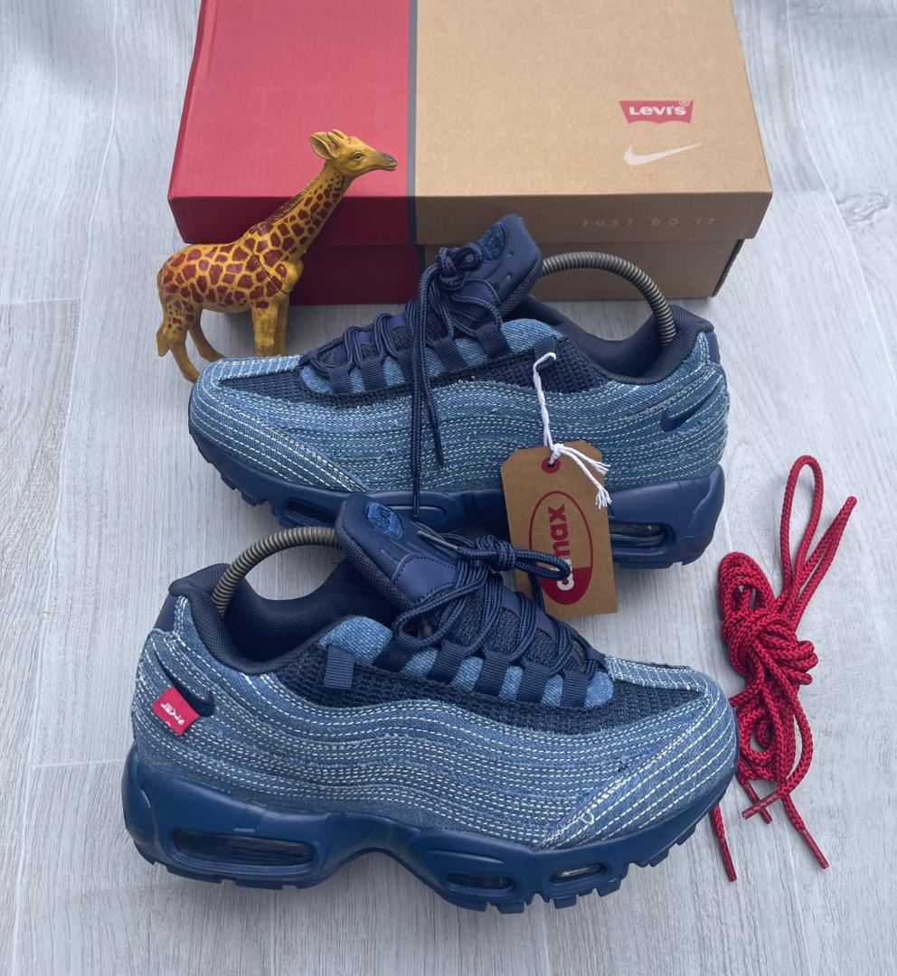 root A pair of denim blue Nike Air Max sneakers with red accents, displayed with a giraffe toy and shoe box on a light grey surface.