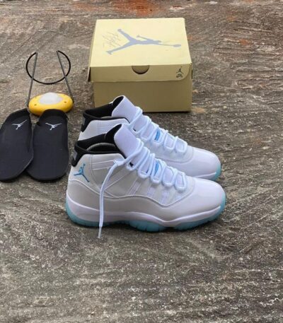 A pair of white and blue Air Jordan 11 Retro sneakers, accompanied by a yellow shoe box and black slides, showcasing the shoe's sleek design and premium packaging.