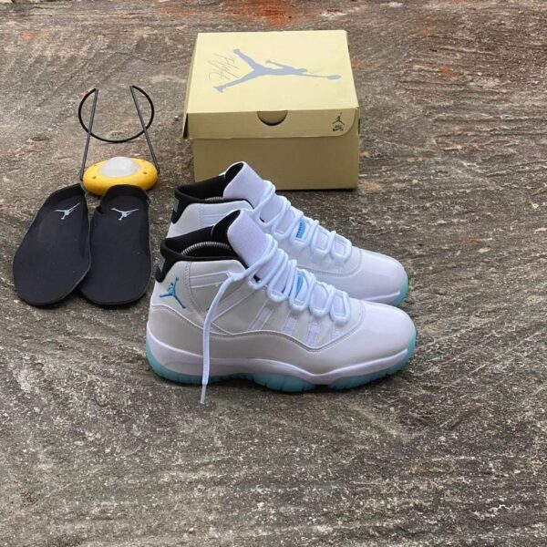 A pair of white and blue Air Jordan 11 Retro sneakers, accompanied by a yellow shoe box and black slides, showcasing the shoe's sleek design and premium packaging.