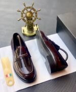 A pair of black patent leather loafers with gold-tone hardware, presented on a white paper with a shoe tree and a black box in the background, embodying the essence of luxury footwear.