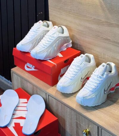 A pair of white sneakers with red accents and black Nike swoosh on a wooden shelf, exuding luxury and style.