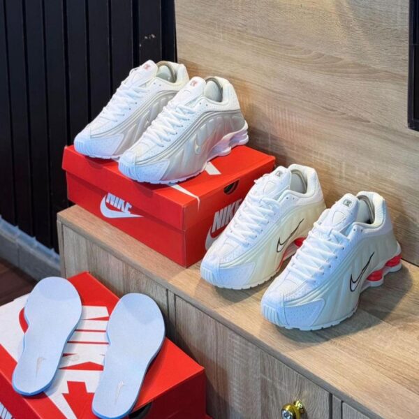 A pair of white sneakers with red accents and black Nike swoosh on a wooden shelf, exuding luxury and style.
