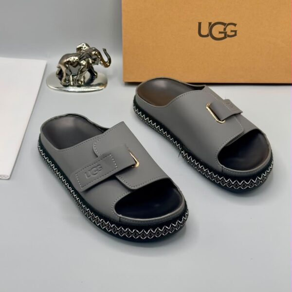 Grey UGG slide sandals with gold accents and stitched sole, presented with a UGG box and luxury accessories.
