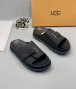 Grey UGG slide sandals with gold accents and stitched sole, presented with a UGG box and luxury accessories.