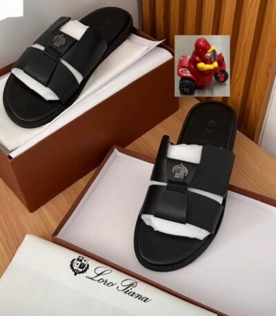 A pair of luxurious black double-strap slide sandals with embroidered logo, presented on a wooden table with a brown shoe box and white tissue paper, embodying comfort and class.