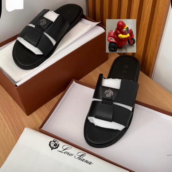A pair of luxurious black double-strap slide sandals with embroidered logo, presented on a wooden table with a brown shoe box and white tissue paper, embodying comfort and class.