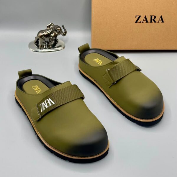 A pair of olive green strap shoes with golden accents, displayed with a silver elephant statue and a Zara box on a white background.