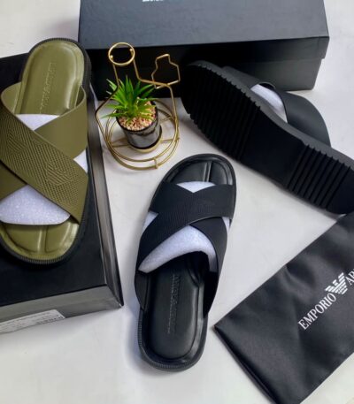 A pair of olive green and black crisscross strap slide sandals on a white surface with their respective boxes and packaging.