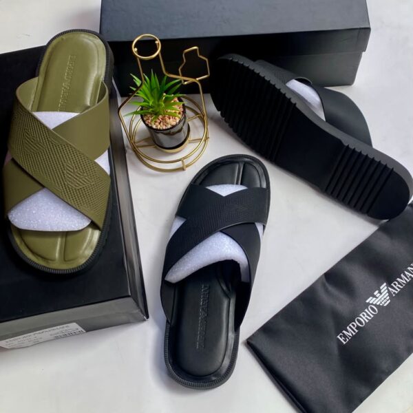 A pair of olive green and black crisscross strap slide sandals on a white surface with their respective boxes and packaging.
