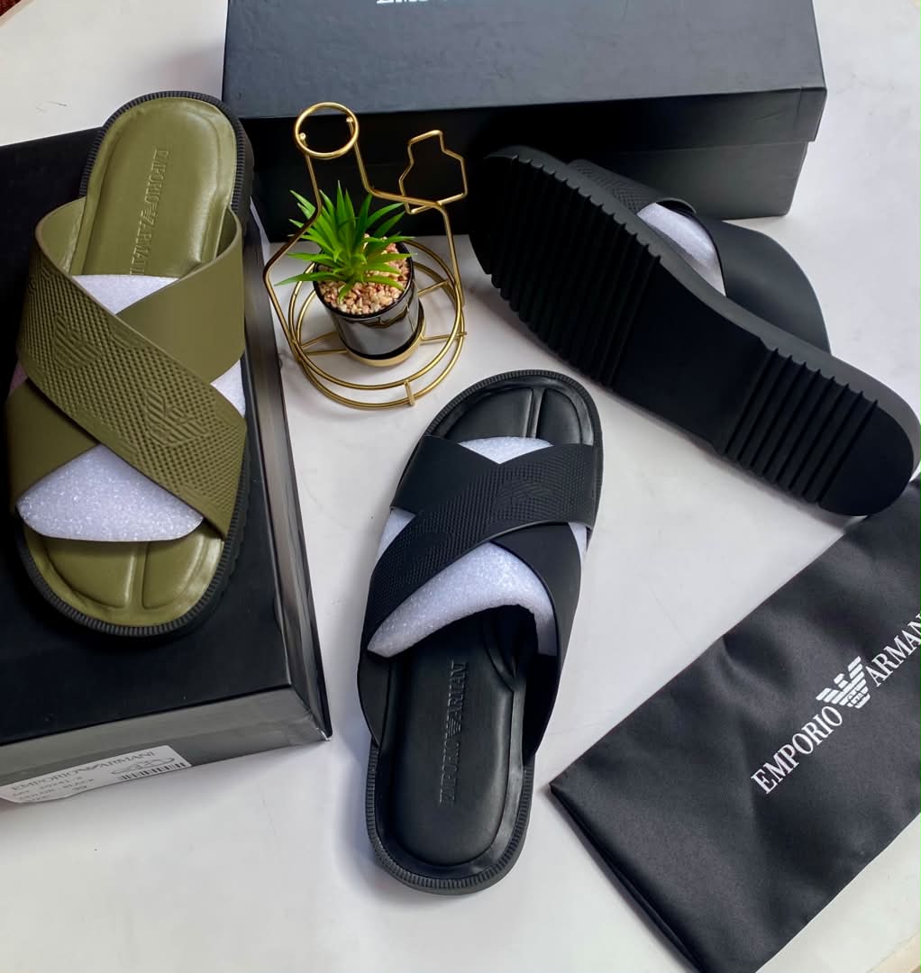 root A pair of olive green and black crisscross strap slide sandals on a white surface with their respective boxes and packaging.
