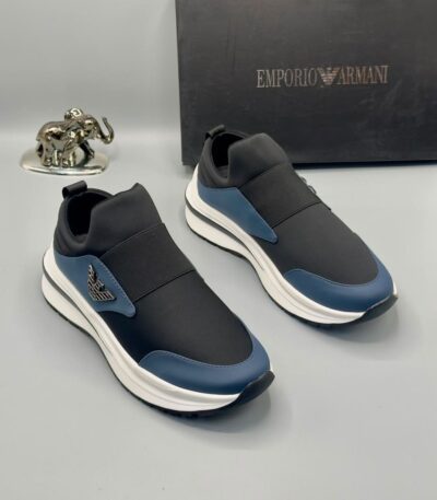 A pair of black and blue Emporio Armani sneakers with white midsole and gold-tone logo, displayed with a black box and silver elephant statue on a gray background.