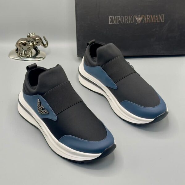 A pair of black and blue Emporio Armani sneakers with white midsole and gold-tone logo, displayed with a black box and silver elephant statue on a gray background.