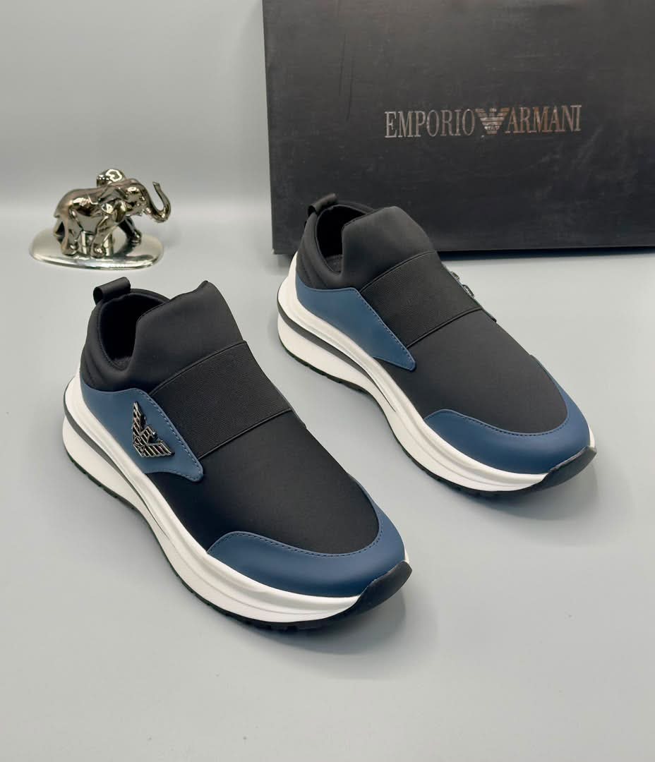 root A pair of black and blue Emporio Armani sneakers with white midsole and gold-tone logo, displayed with a black box and silver elephant statue on a gray background.