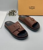 Grey UGG slide sandals with gold accents and stitched sole, presented with a UGG box and luxury accessories.