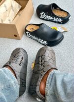 A pair of stylish black and grey shoes with distinctive designs, placed on a grey surface next to a shoe box.