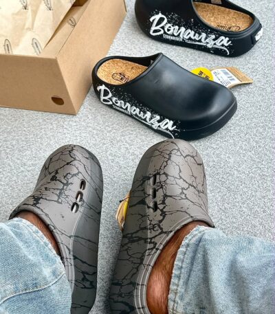 A pair of stylish black and grey shoes with distinctive designs, placed on a grey surface next to a shoe box.